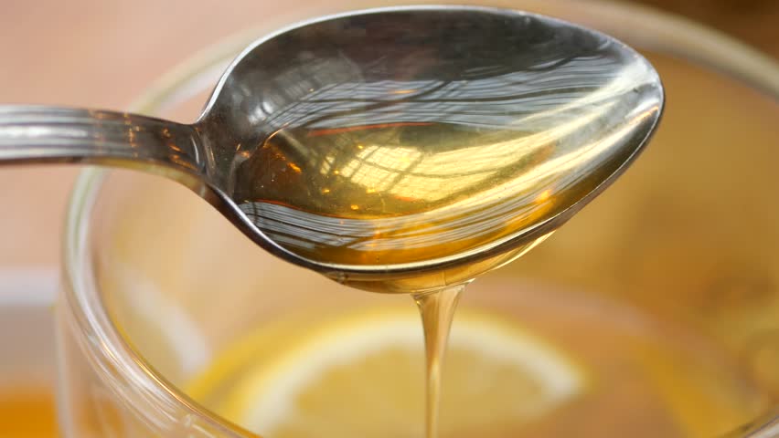  pouring honey in a cup of tea on table 