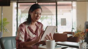 Medium shot of positive Asian woman wearing earphones using digital tablet in restaurant after work - Powered by Shutterstock - Get 15% off with code: PIKWIZARD15