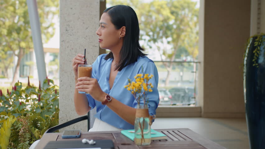 Elegant Asian businesswoman having iced coffee during outdoor breakfast in cafe