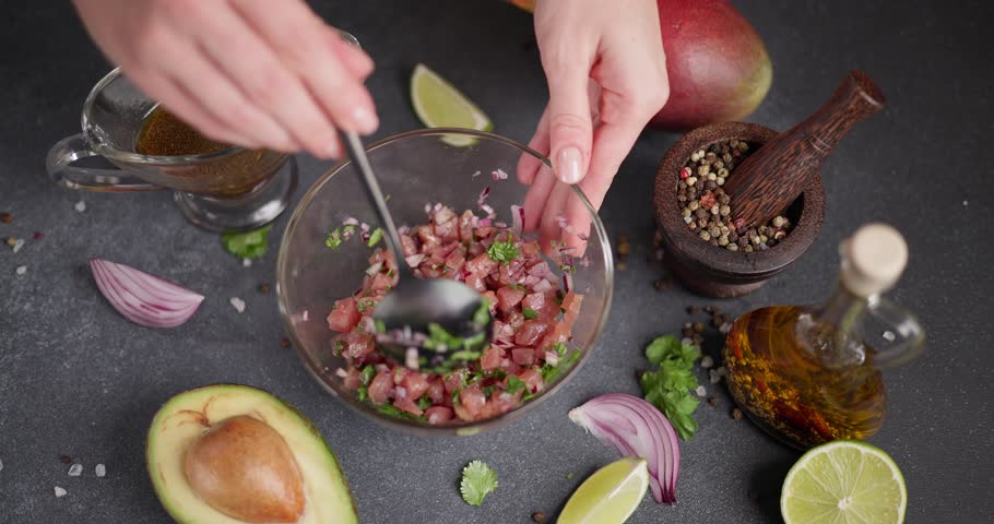 Woman mixing chopped tuna, cilantro and onion in a glass bowl cooking traditional tuna tartare