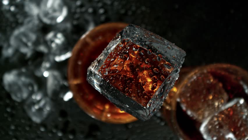 Super Slow Motion Shot of Ice Falling into Fresh Cola Lemonade Followed by Camera at 1000fps.