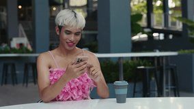Happy Transgender Woman With Blonde Hair Wearing Pink Feather Top, Smiling While Using Smartphone At Outdoor Cafe. LGBT Person With A Coffee Cup On Table - Powered by Shutterstock - Get 15% off with code: PIKWIZARD15