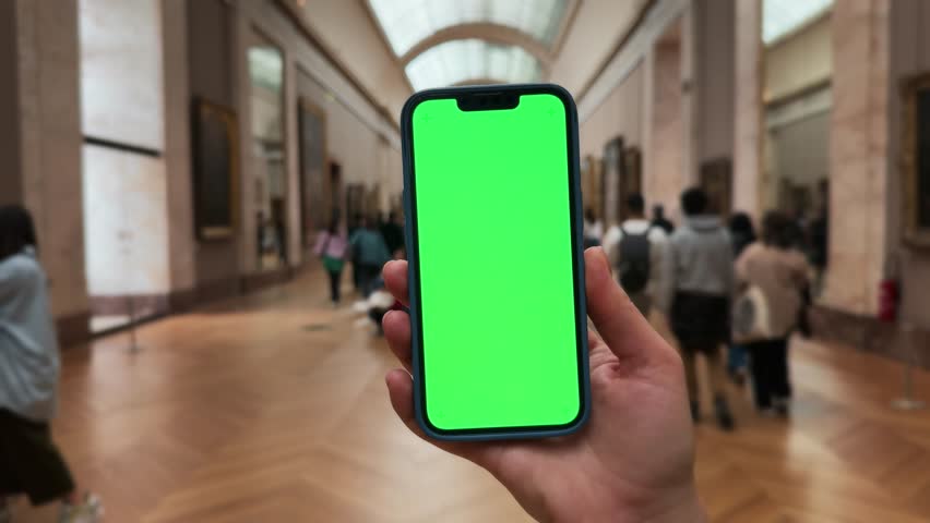 Mobile phone in hand. Man holding smartphone with green screen chroma key on museum gallery background.