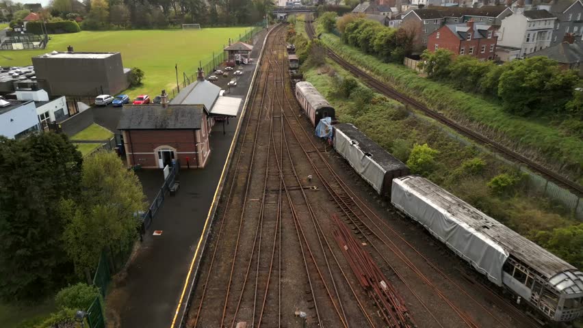 Aerial of a vintage railway station in Whitehead, Northern Ireland. The camera moves forward showing the tracks, signal box and trains. Produced in 4K, 60 frames per second and Rec709 color space.