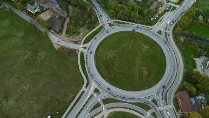 Aerial view of a roundabout in countryside with smooth traffic flow, roads, vehicles passing through green fields