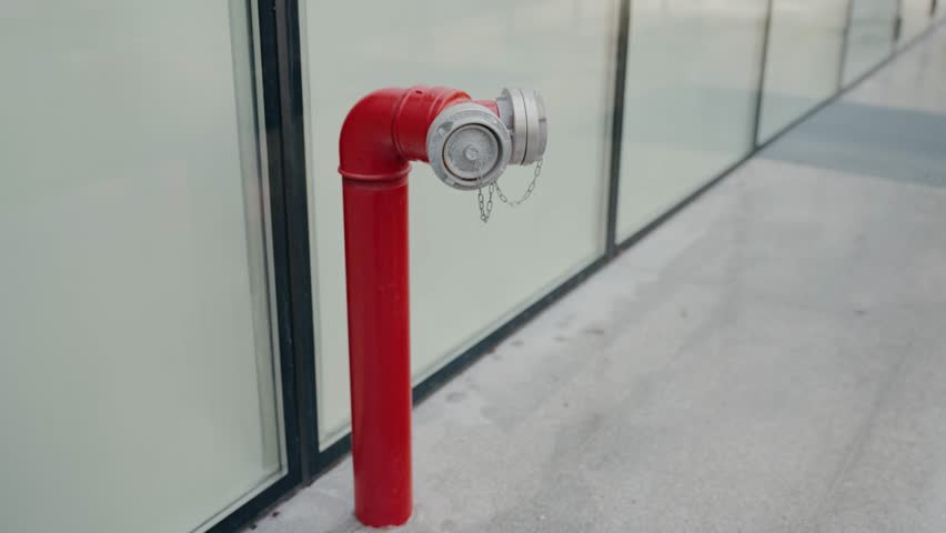 A bright red fire hydrant stands out on a city sidewalk, with a modern, glass paneled building in the background. Red Fire Hydrant on a City Sidewalk, Modern Building Background