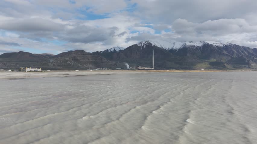 Wide high orbit aerial view of the Great Salt Lake, Utah with large copper mine smelter in the background on a sunny day.