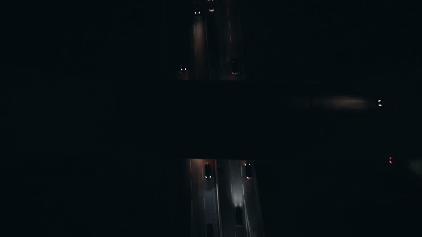 Top view highway interchange at night with car traffic in Dartmouth, Canada. Cars drive in the dark, their headlights illuminating the path ahead in stark contrast to the surrounding darkness.