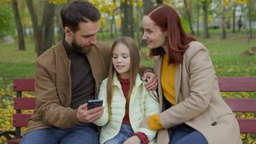 Caucasian happy smiling family relax weekend holiday on city bench autumn park using mobile phone together smile app shopping online smartphone talking little daughter girl child kid mother father - Powered by Shutterstock - Get 15% off with code: PIKWIZARD15