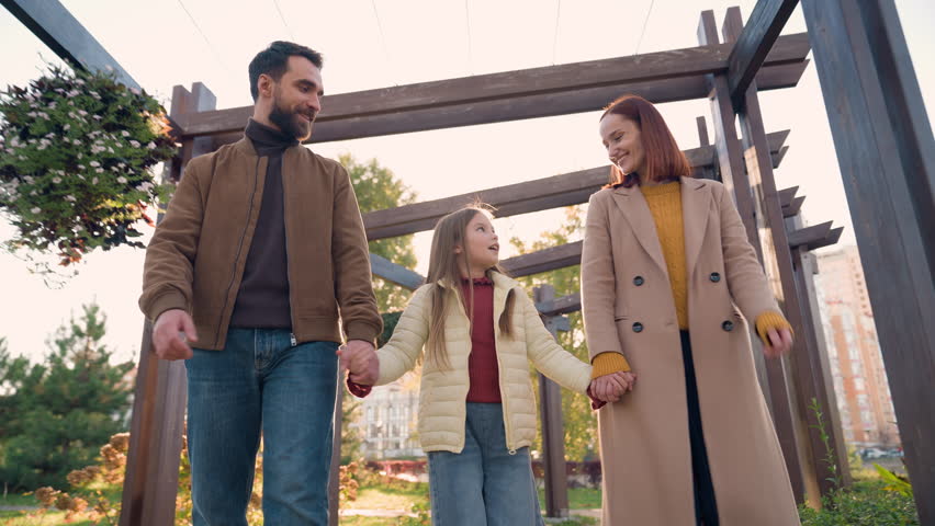 Caucasian happy smiling family relax weekend holiday outdoors in sunny city autumn park together smile talking little daughter girl child kid with parents mother woman father man holding hands walking