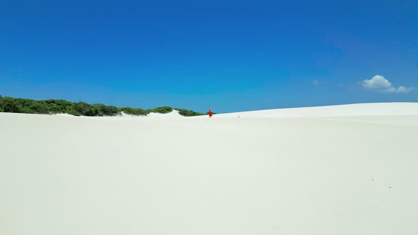 Woman in red dress on white sand dunes in Brazil desert in Lencois Maranhenses. Attractive young woman in red dress. Aerial drone view.