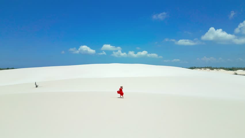 Woman in red dress on white sand dunes in Brazil desert in Lencois Maranhenses. Attractive young woman in red dress. Aerial drone view.