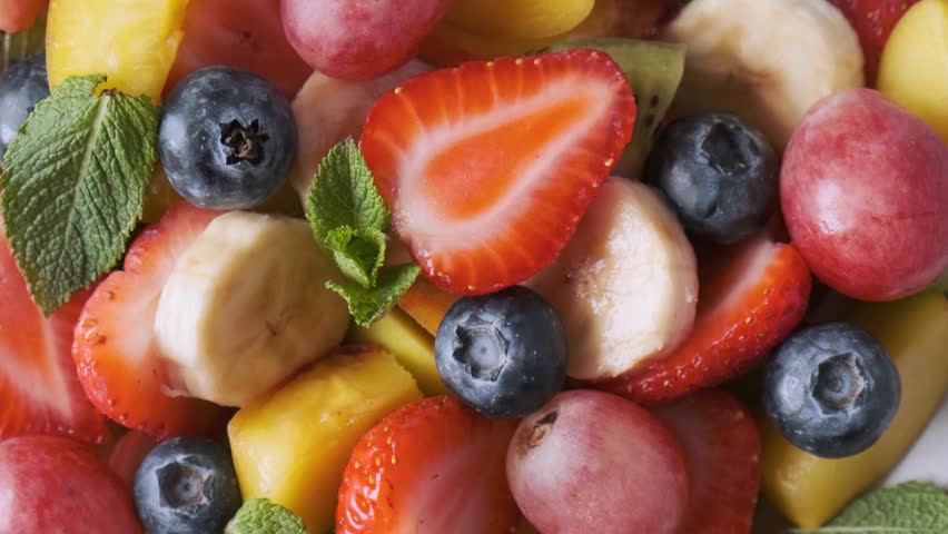 Healthy fresh fruit salad in a bowl on pink background. Top view. Summer healthy food for breakfast. Mixed tropical fruits berries for vegan diet lunch. Close up