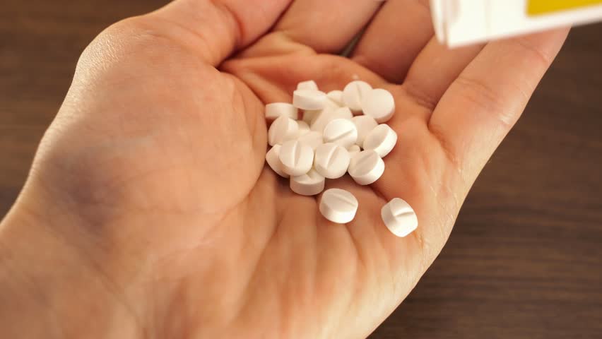 White pills (drugs) falling into the hand palm from white container