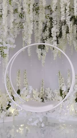 Round hanging swing among flowers in white style for wedding photo shoot of newlyweds.