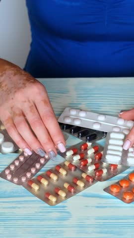Close-up of a woman's hands selecting the right blister with pills among different. The skin disease vitiligo is a dermatologic disease.