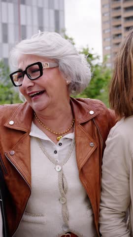 Vertical. Group of three mature caucasian women enjoying embracing walk together laughing outdoor. Senior female friend having fun hugging strolling happy urban city street. Elderly people golden ager