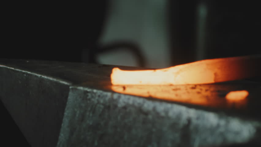 Person hitting hot smelted metal and causing flying sparks over an anvil