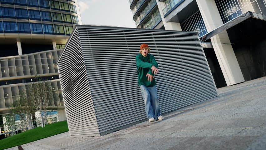 Dancing young hip hop dancer wearing green hoodie performing freestyle dance moves in city