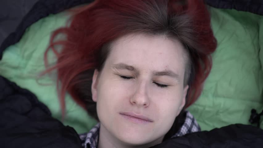 A woman tourist sleeps in a sleeping bag, close-up. A frightened woman wakes up from a nightmare in her sleep