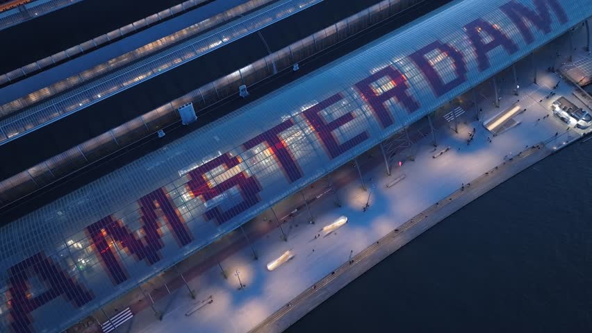 The drone is flying up tilting up looking at the Amsterdam Central train station at night in Amsterdam The Netherlands Aerial Footage 4K