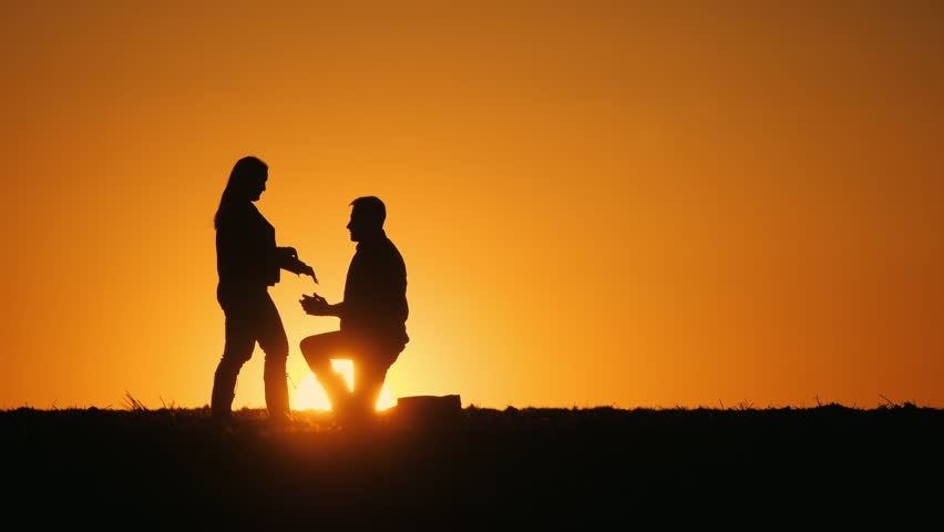 Silhouettes of a romantic couple at sunset. A man proposes marriage