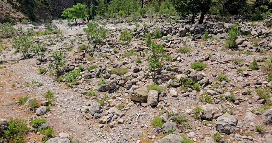 Samaria Gorge landscape view of dry riverbed and vertical cliffs, tourists hiking through the gorge, Crete, Greece.