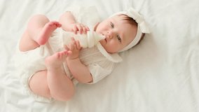Newborn baby girl sucks a bottle of milk in white clothes on the bed at home on her back, cute baby eats, space for text - Powered by Shutterstock - Get 15% off with code: PIKWIZARD15