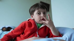Young boy in red hoodie with finger to his lips, lying on a bed, looking curious - Powered by Shutterstock - Get 15% off with code: PIKWIZARD15