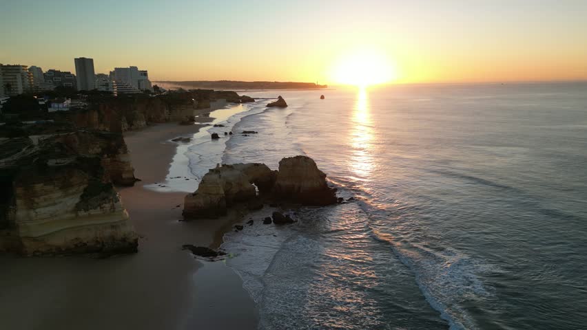 Aerial view of Praia dos Tres Castelos at sunset with rocky cliffs and ocean waves, Portimao, Algarve, Portugal.