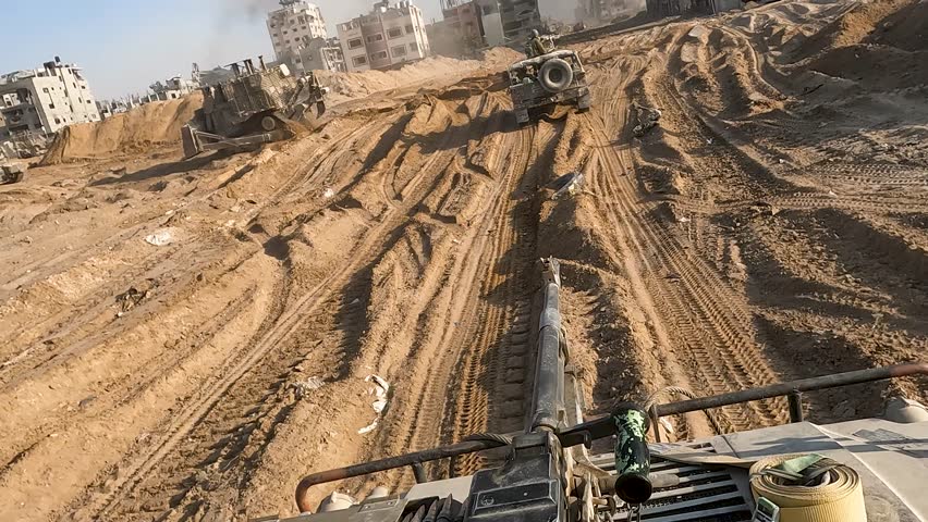  Armoured Bulldozers move across sand supported by two Humvee close to built up area 