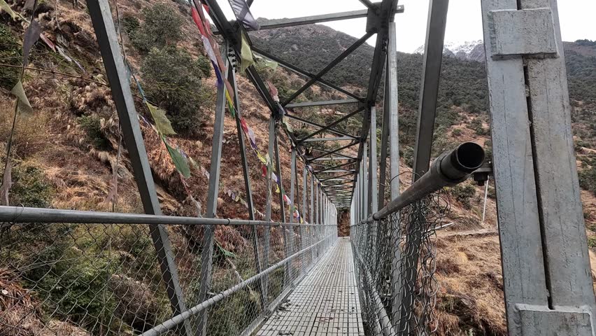 Crossing a metal hiking bridge with buddhist prayer flags. Lower Langtang Valley Trek in Nepal