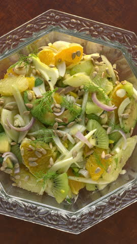 Fennel salad with citrus and avocado in a cristal glass bowl. Table spin. Zoom in while rotating. Vertical video.