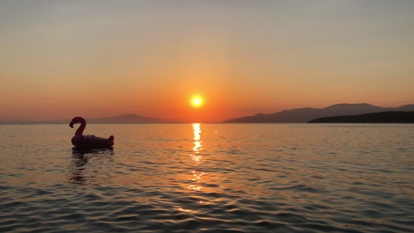 An inflatable flamingo drifts peacefully on calm waters at the beach during a tranquil sunset, creating a serene and picturesque scene.