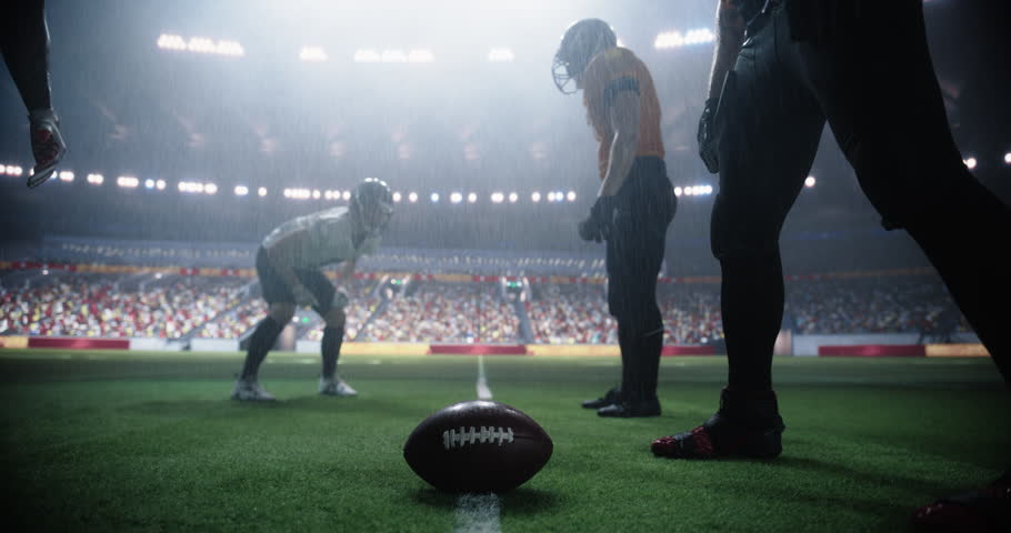 Two Diverse American Football Teams Play a Dynamic Match in Soaking Wet Weather in Front of a Stadium Filled with Spectators. Players Making a Stand-Off Before Quarterback Passes the Ball