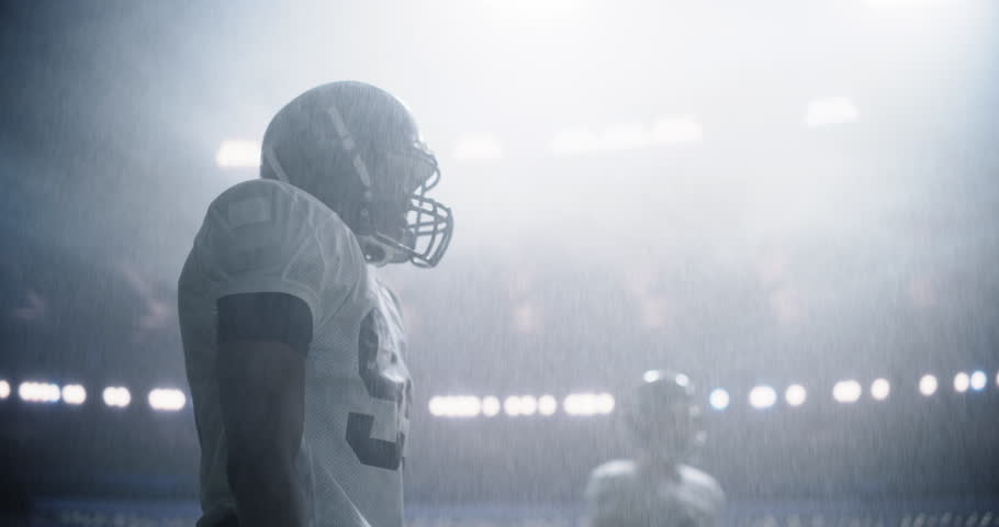 Portrait of Two Diverse American Football Teams Playing Ball with a Heavy Rain Forecast. Cinematic Footage of Strong Athletic Footballers in Professional Uniform Holding Each Other as the Game Starts