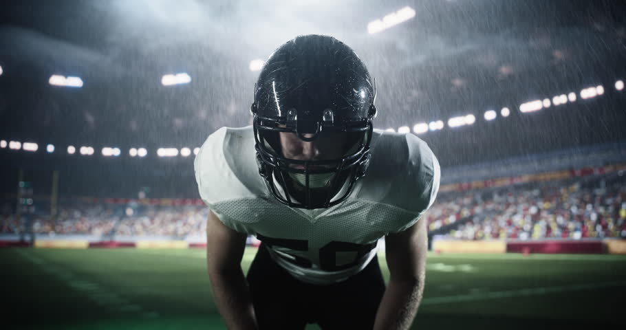 Focused Caucasian Male American Football Player Wearing a Helmet and Uniform. Close Up Portrait of a Footballer on a Stadium Field in Rainy Conditions, Standing in a Position for a Game to Start