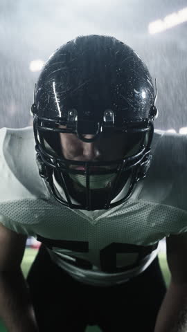 Vertical Screen: Focused American Football Player Wearing a Helmet and Uniform. Close Up Portrait of a Footballer on a Stadium Field in Rainy Conditions, Standing in a Position for a Game to Start