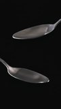 White sweet condensed milk sauce flowing from metal spoon on black background. Food close up, slow motion, vertical video 4K