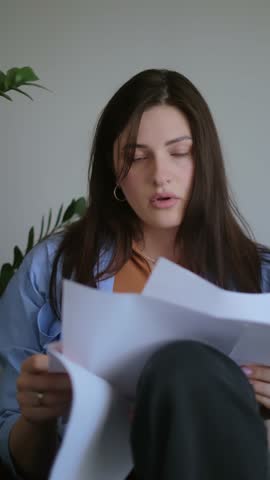 Woman in a blue shirt reviewing documents, working from home on paperwork for freelancers and creative professionals, project planning, and time management.