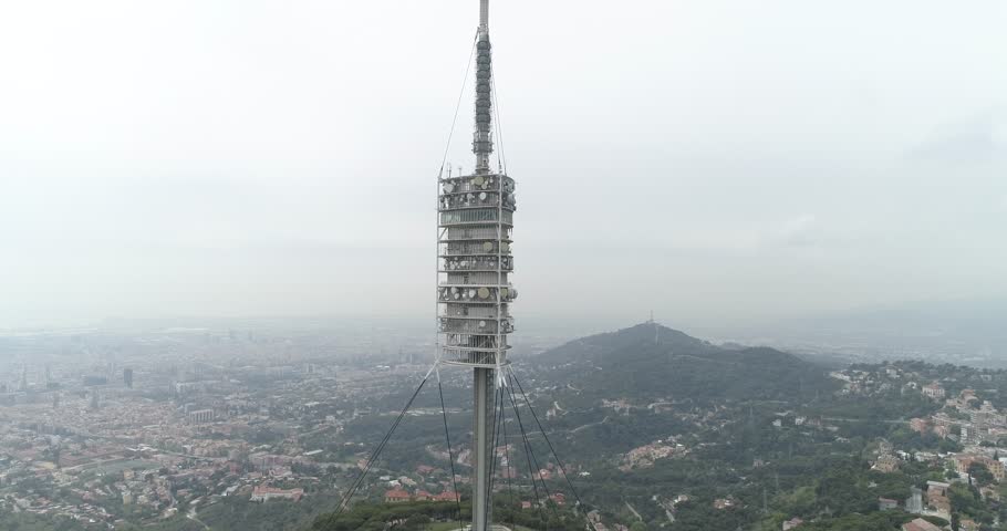 Aerial view of Collserola television tower on Tibidabo mountain in Barcelona city. Drone view with a cityscape in the background. Travelling up and tilt down movement.