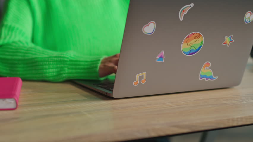 Female hands typing on keyboard of laptop with lgbt rainbow stickers in office