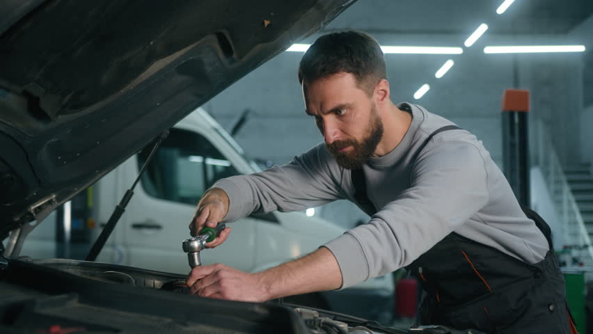 Car mechanic vehicle service worker working in workshop garage using wrench tool to repair engine open hood automobile adult Caucasian man auto engineer in technical uniform happy looking camera smile