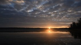 Time lapse of heavy early morning clouds moving above a very calm lake. The sun rises above the horizon at the end of the clip.  The calm water creates a perfect reflection.  Trees line the distant sh - Powered by Shutterstock - Get 15% off with code: PIKWIZARD15