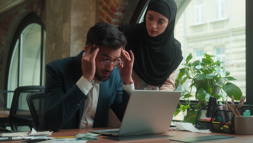 Arabian Indian businessman male business man feel headache working laptop at office tired guy suffer migraine pain head ache Muslim woman in hijab businesswoman help drink glass water medical health