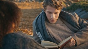 Happy man reading book aloud lying on picnic blanket at nature closeup. Relaxed young couple enjoying novel in autumn beach. Carefree family discussing literature chilling together. Weekend leisure  - Powered by Shutterstock - Get 15% off with code: PIKWIZARD15