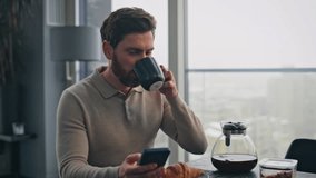 Busy businessman pouring coffee cup at panoramic windows kitchen closeup. Focused man watching mobile phone taking cappuccino sip. Serious bearded guy reading social media enjoying breakfast at flat - Powered by Shutterstock - Get 15% off with code: PIKWIZARD15
