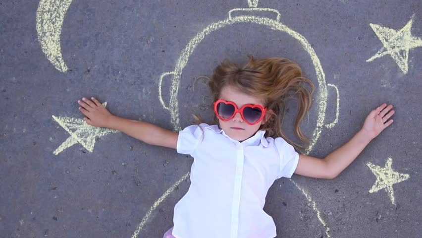 A little child is pretending to be an astronaut outside with creative chalk drawings of the stars and moon for an education or imagination concept.