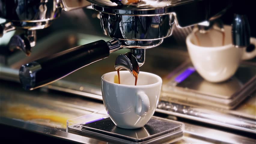 Close-up of the Espresso coffee extraction from a professional coffee machine with a bottomless filter. Coffee flowing into cup. Coffee aroma and the warm shop atmosphere