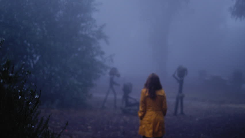 Woman in a yellow coat walking towards an artists statue on a foggy day